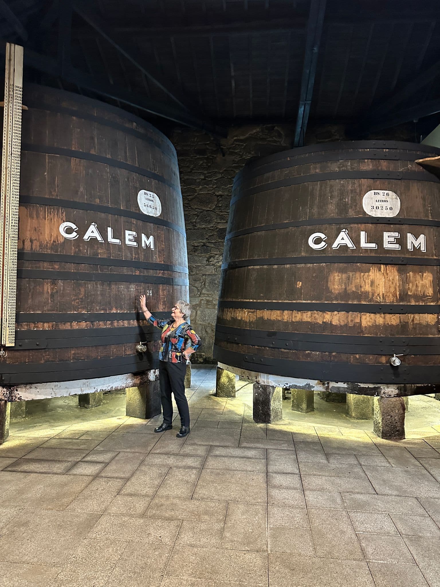 Large wooden port wine barrels at Cálem Cellars, Vila Nova de Gaia, Porto, Portugal, with a visitor reaching up to touch one.