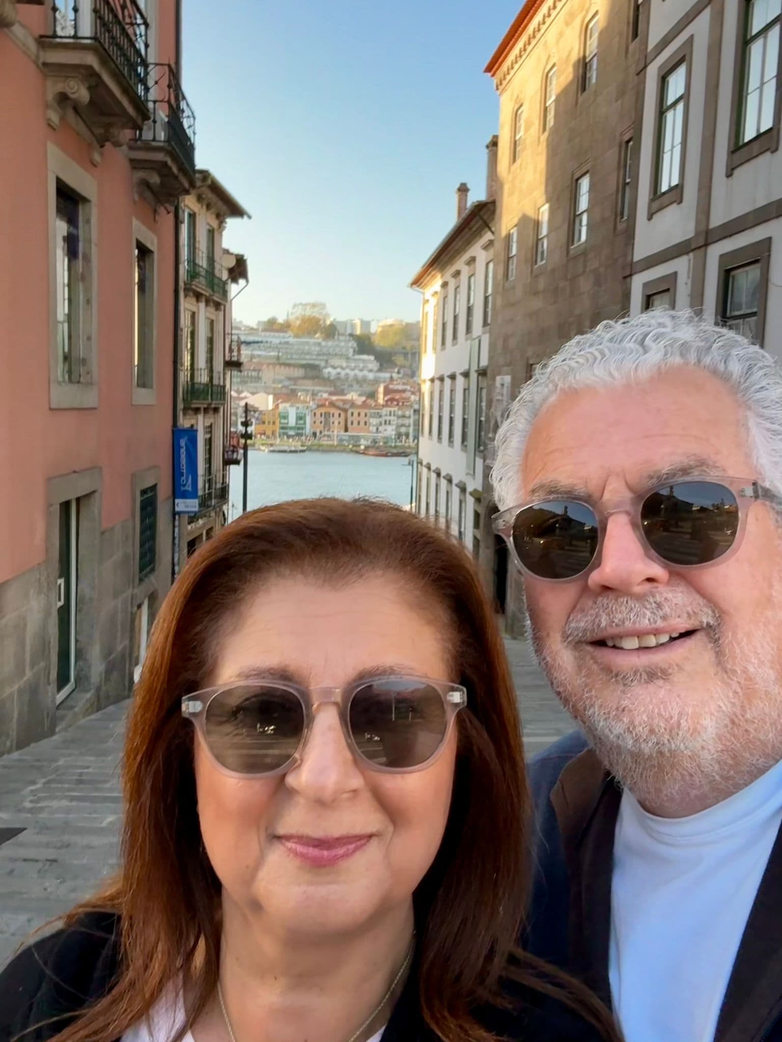 Ribeira waterfront in Porto with two travelers taking a selfie on a narrow street, Douro River and colorful riverside buildings behind them, Portugal.