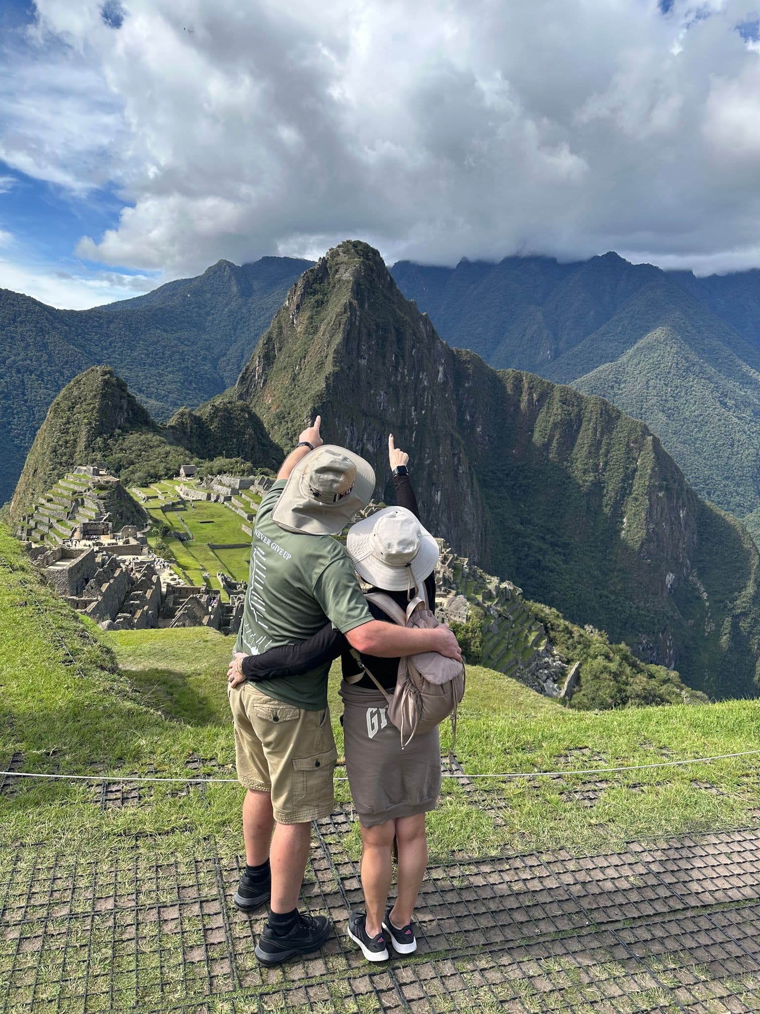 Machu Picchu terraces and Huayna Picchu peak with two travelers embracing and pointing, Cusco Region, Peru.