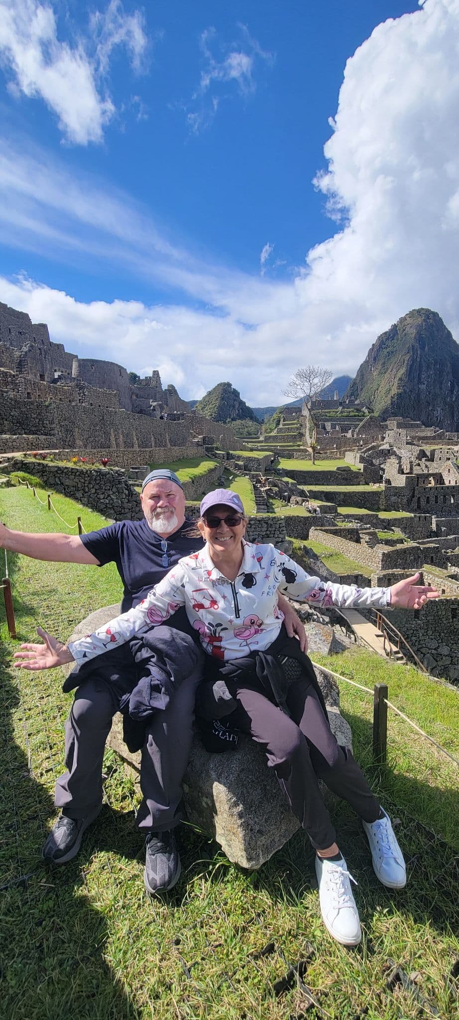 Machu Picchu ruins with two travelers sitting on a stone with arms outstretched, Cusco region, Peru