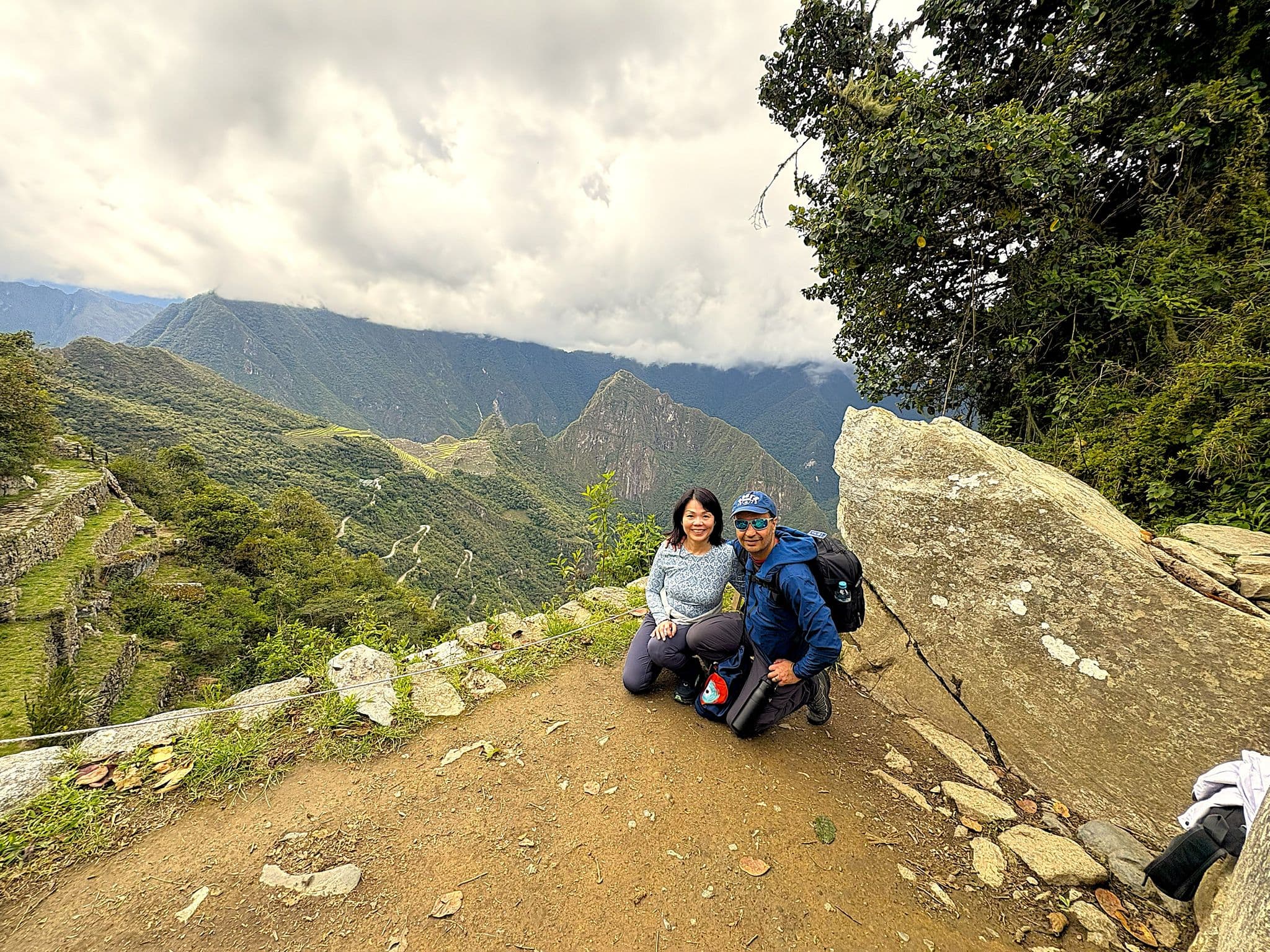 Machu Picchu terraces and mountains with two hikers kneeling at a viewpoint on the Inca Trail, Cusco region, Peru.