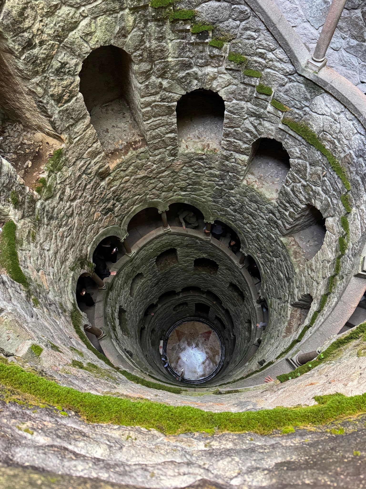 Initiation Well spiral stone shaft at Quinta da Regaleira, Sintra, Portugal, viewed from above with visitors on the walkway.