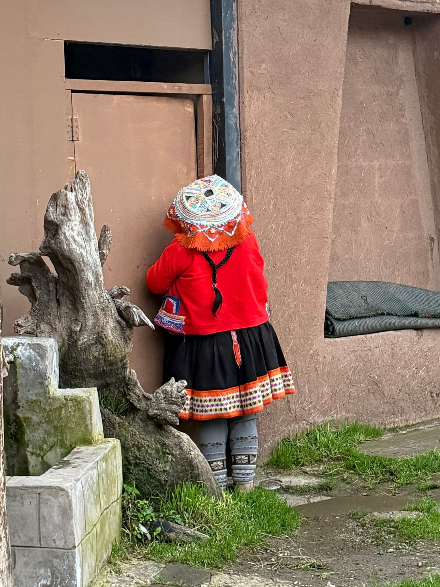 Person in a red jacket and embroidered hat standing at a doorway in the Sacred Valley, Cusco, Peru.