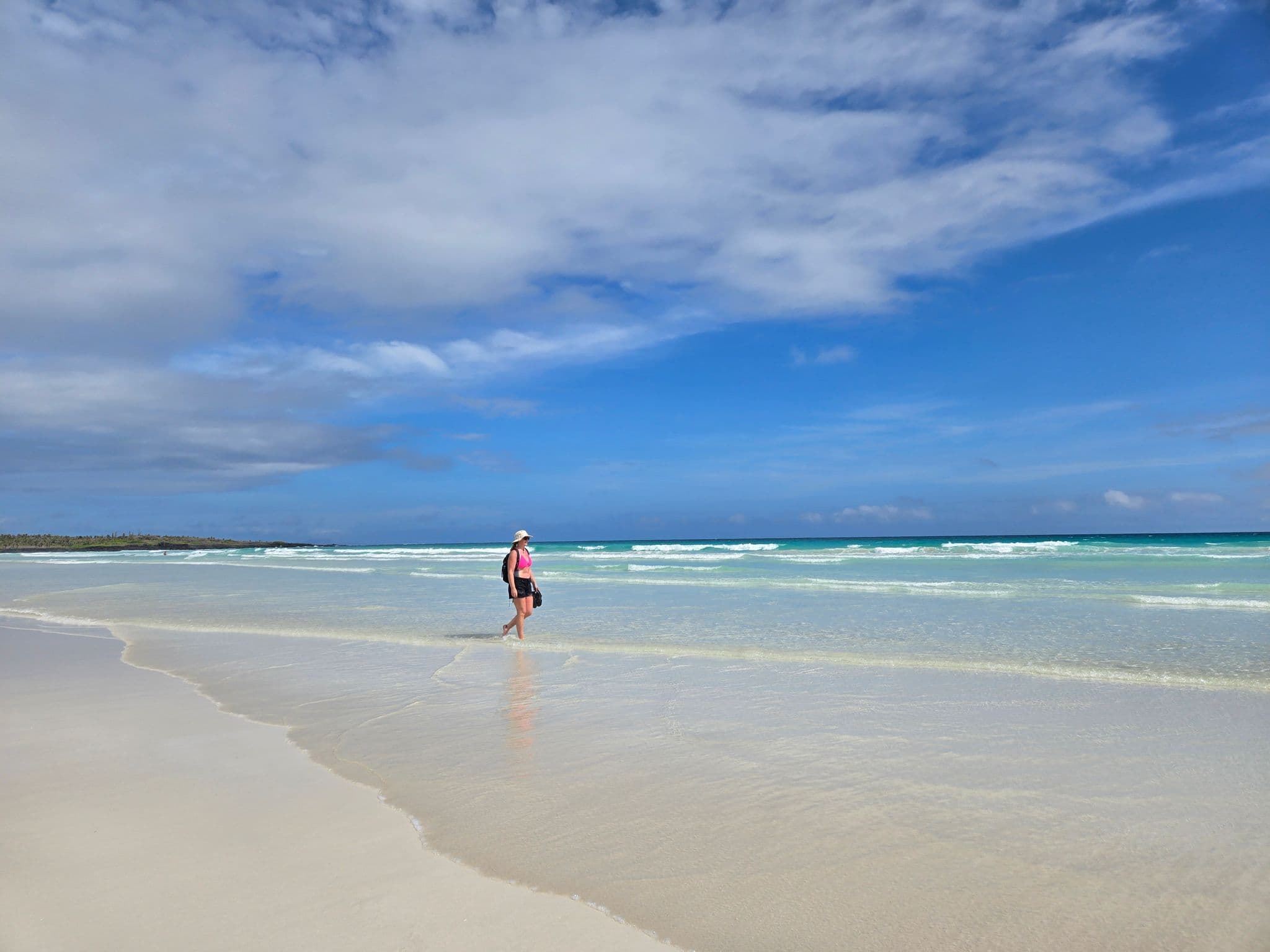 Tortuga Bay beach shoreline with a person walking in shallow turquoise surf, Santa Cruz, Galápagos, Ecuador.