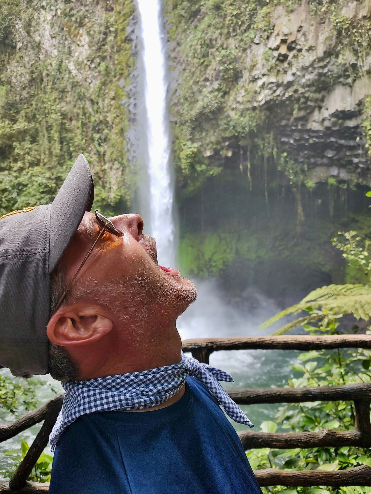La Fortuna Waterfall in Arenal, Costa Rica, with a man on a viewing platform tilting his head and pretending to drink the falling water.
