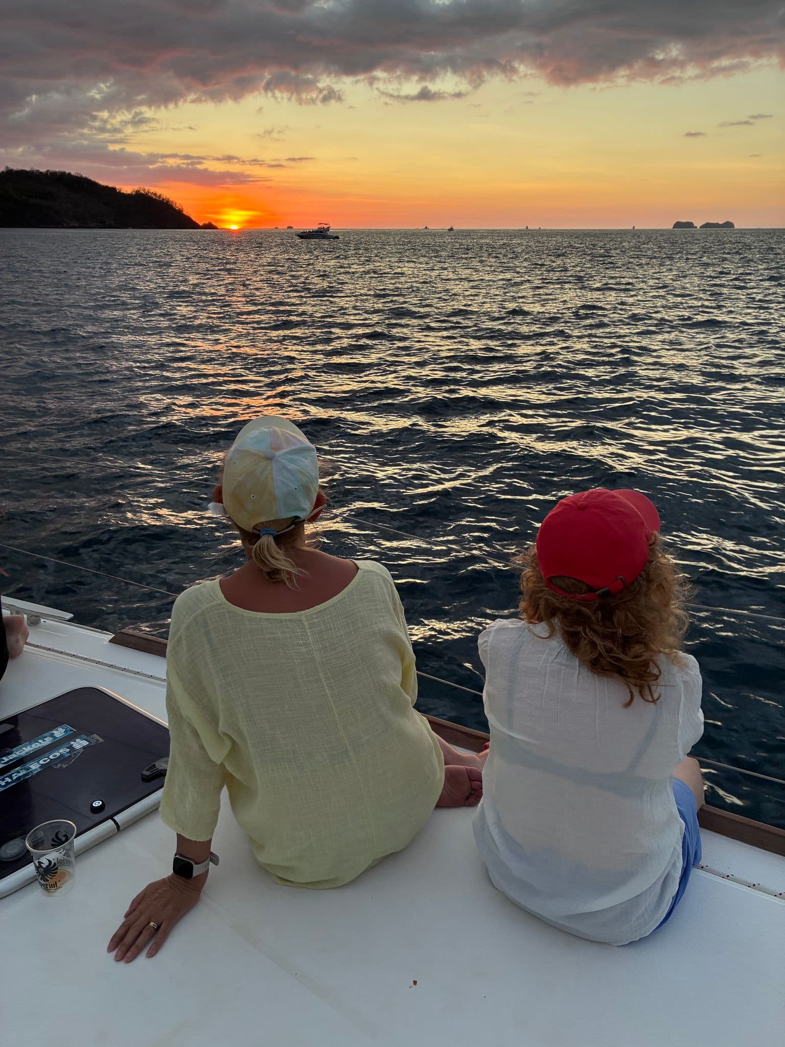 Two women sitting on a boat watching the sunset over the ocean off Costa Rica during a trip.