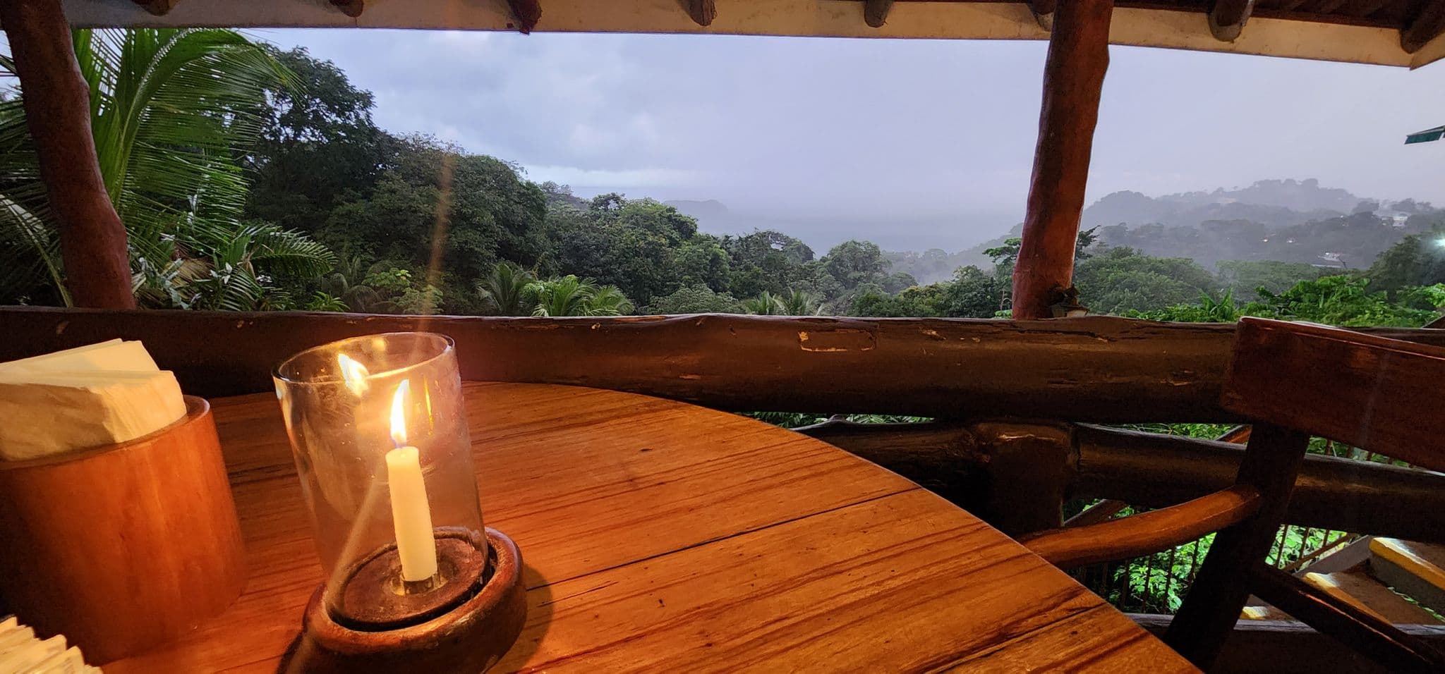 Candlelit wooden table on a covered balcony overlooking misty rainforest and the distant Pacific coast, Costa Rica.